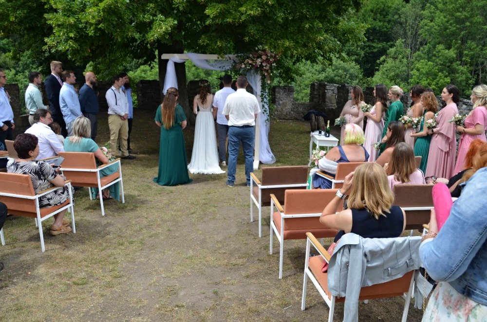 Hosté sledují svatební obřad pod korunami stromů na hradě